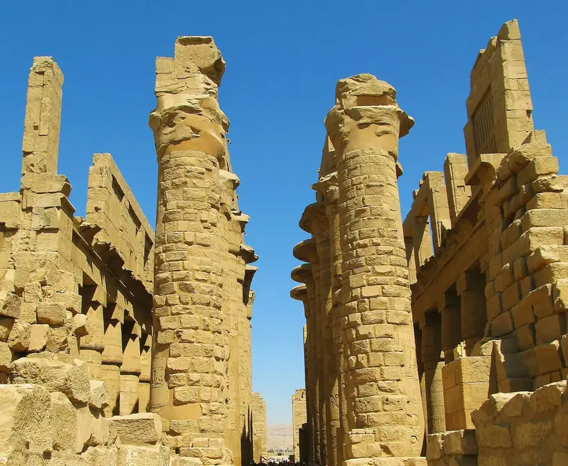 Colunas da sala hipostila do templo de Karnak cobertas de relevos, contra um céu azul